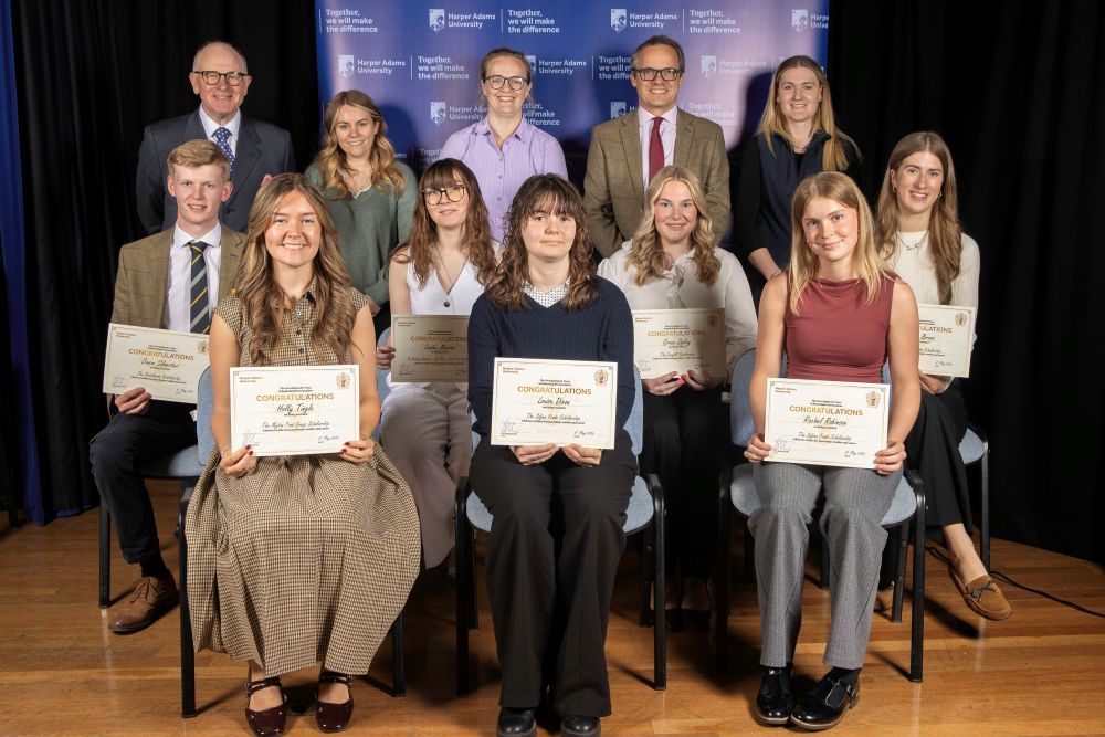 Two rows of seated students holding certificates, with a row of people standing behind them.